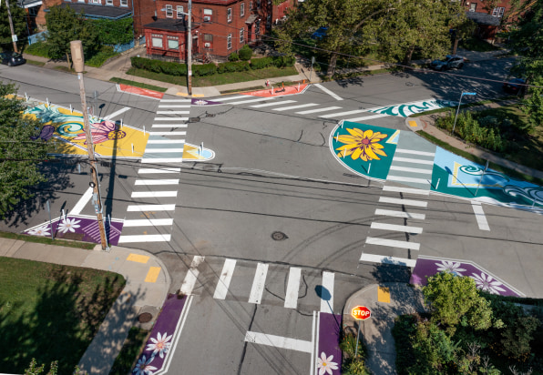 Aerial view of an intersection where bright artworks are painted on the corners of the intersection. 