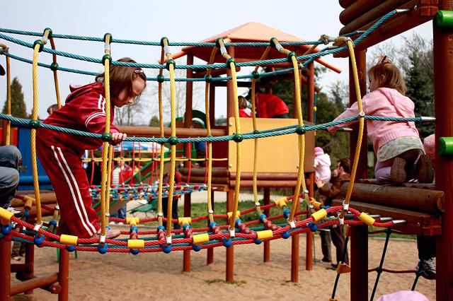 Two children are climbing on a rope web obstacle course. 