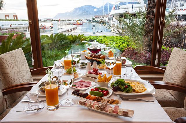 A restaurnt table laid with breakfast foods. It looks out to a water view with small boats. 