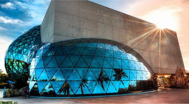 View of the outside of the museum showing two large blue egg shapes attached to a concrete rectangle. Together they form the shape of the building.