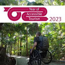 A man in a wheelchair makes his way along a paved pathway amongst palm trees. The text says, Year of Accessible Tourism.