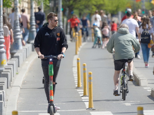 A cycle-way divided by yellow bollards with a man on an e-scooter and a man on bicycle travelling in opposite directions. Pedestrians are visible on the separated footway.