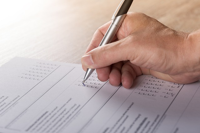 A hand holding a pen poised on a questionnaire form ready to check a box on the form. There is lots of lines of text and check boxes. 