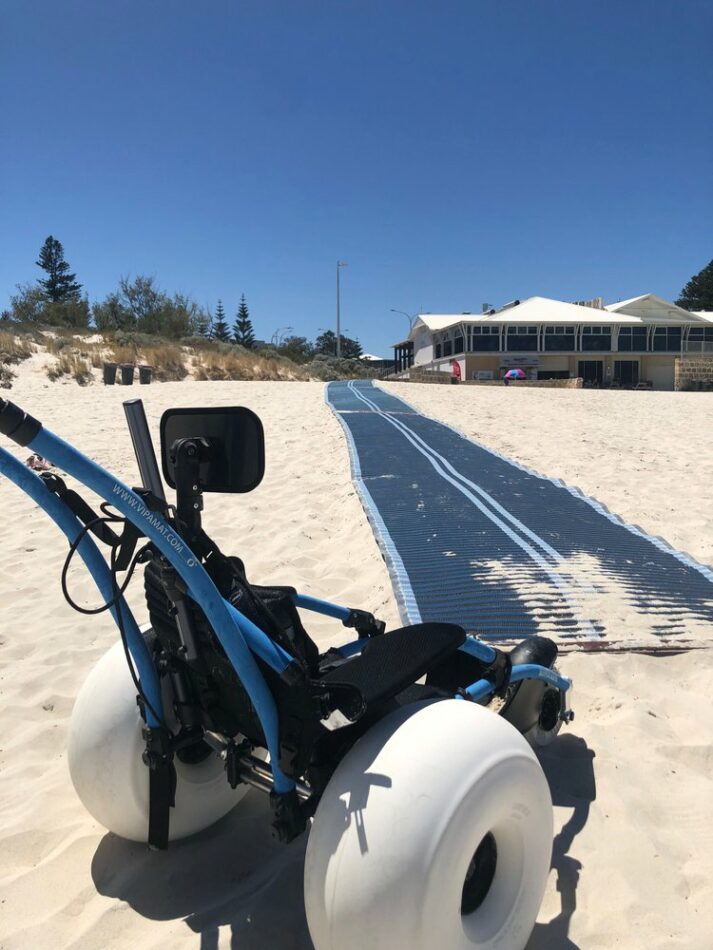 A beach wheelchair at the end of matting on the beach. 