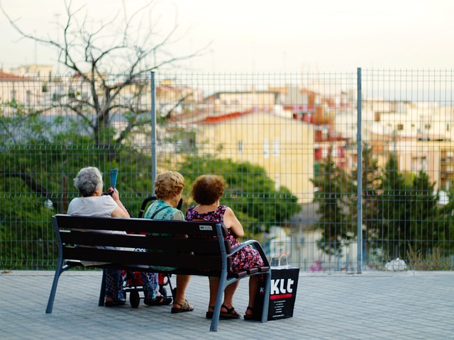 Three older women are sitting on a public seat overlooking some housing in the distance.  Older people and smart  cities.